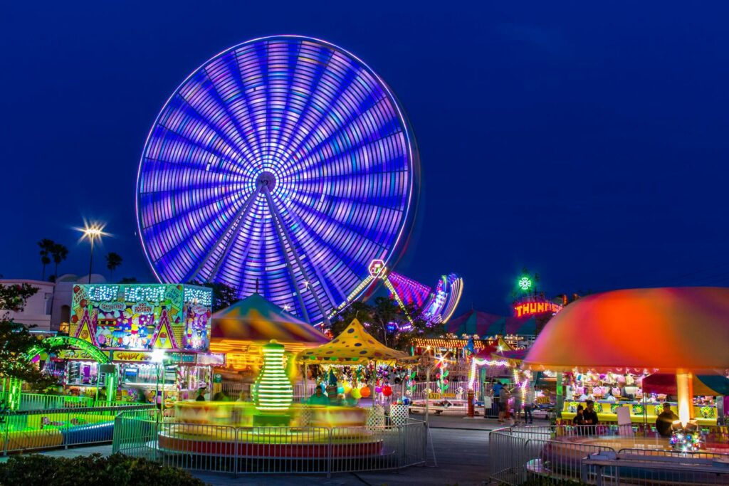 Brightly lit amusement park with a spinning Ferris wheel at night.